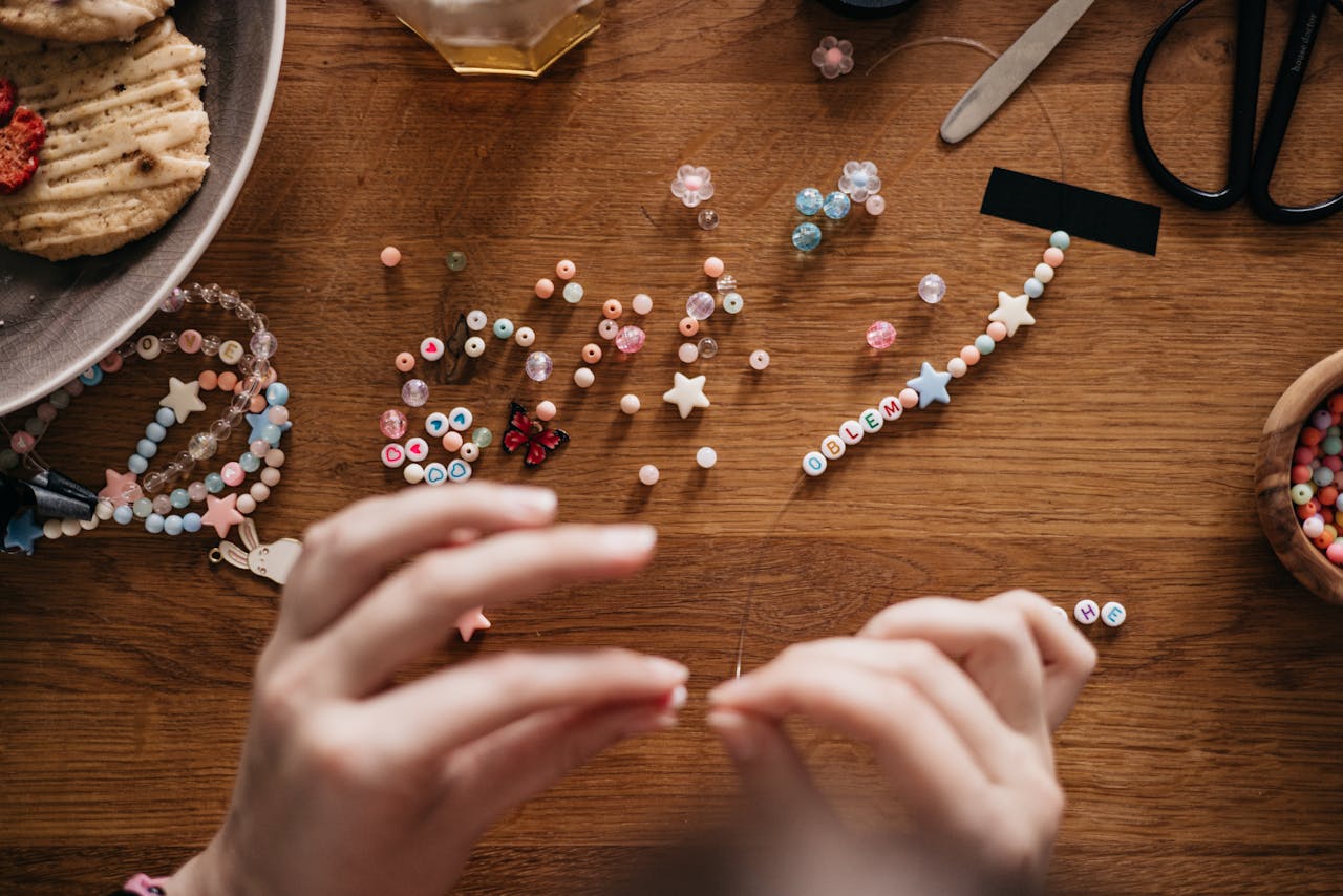 Hands crafting personalized jewelry with beads at a well-organized wooden table.